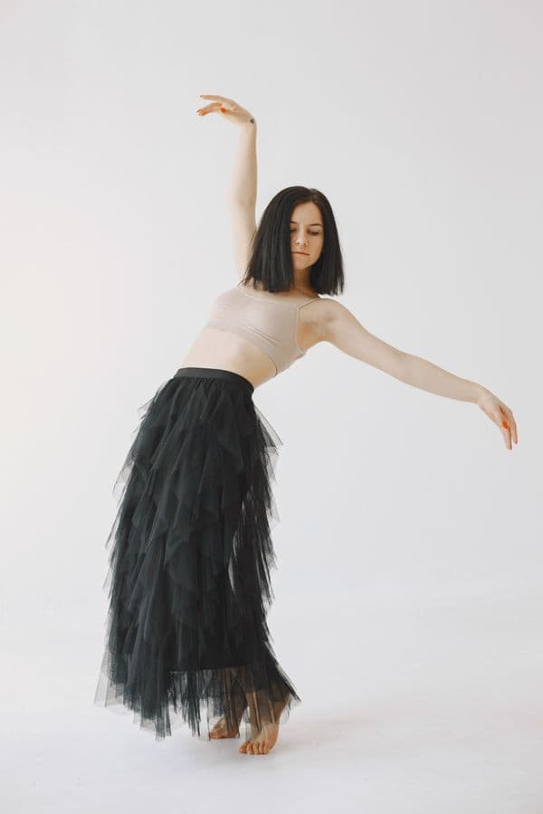 A dancer in a black skirt leaning to one side, with one arm raised and the other extended.